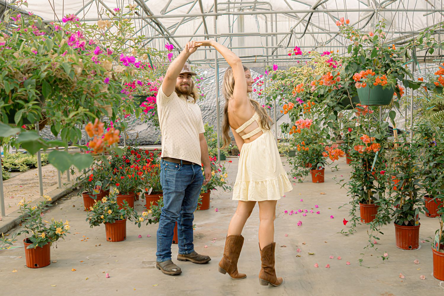 Couple dancing together in a lush greenhouse surrounded by colorful flowers and potted plants.