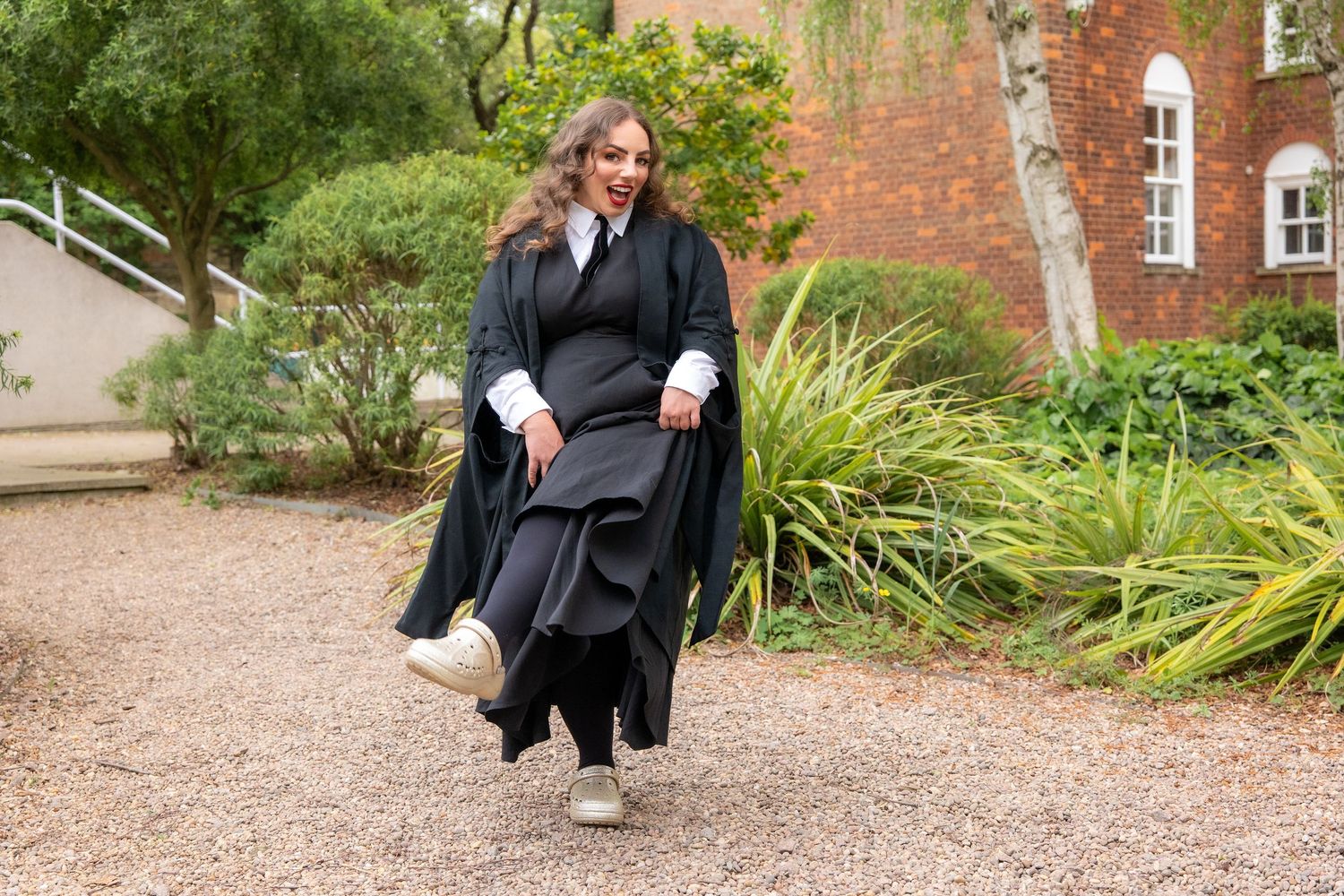 Graduate in academic gown holds bouquet of flowers with family outside historic stone building.