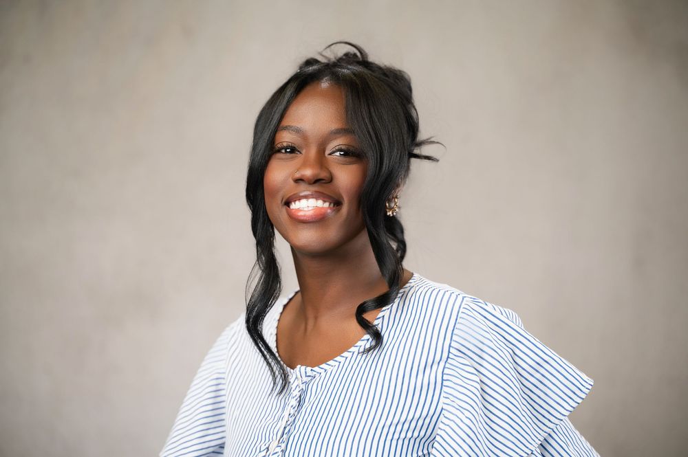 Smiling young Black woman in a blue striped ruffled blouse poses for a professional portrait photo.