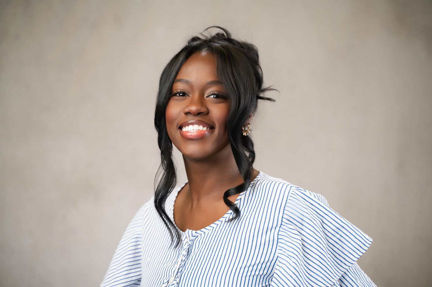 Smiling young Black woman in a blue striped ruffled blouse poses for a professional portrait photo.