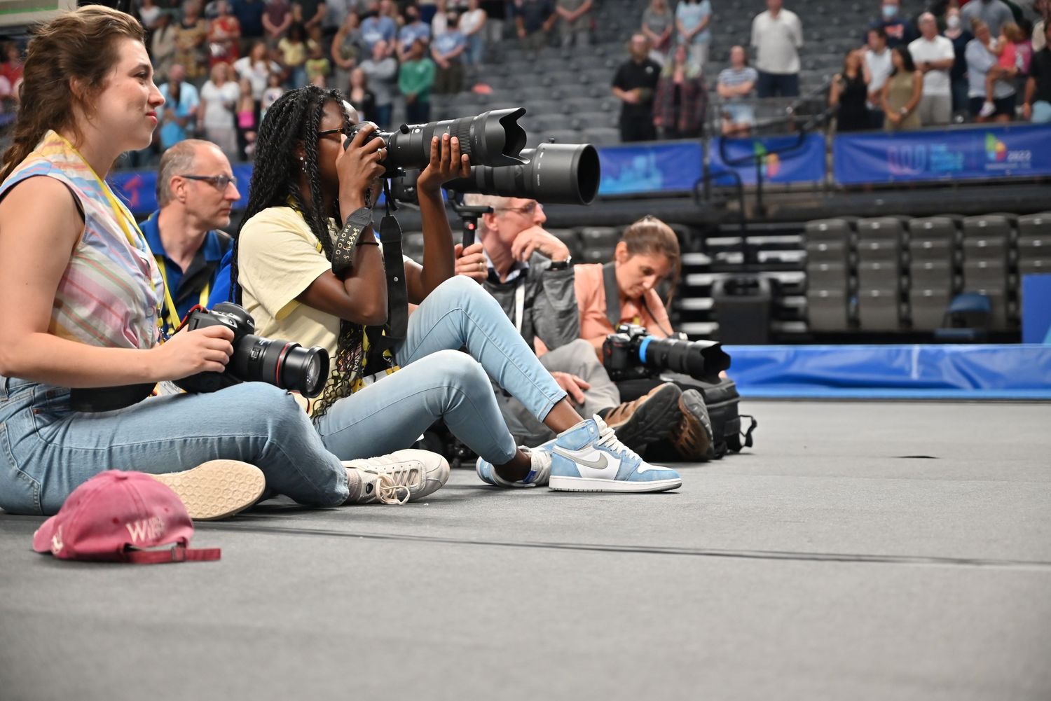 Photographers sitting on arena floor with cameras at a sports event.