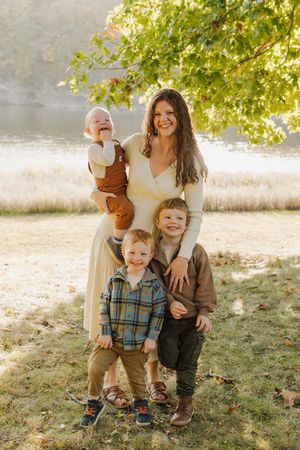 A family poses together on a sunny autumn day by a lake with golden light filtering through tree branches.