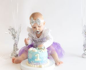 A series of photos showing a first birthday cake smash session with blue frosted cake and silver decorations.