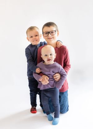 Three children stand together against a white background in casual clothing.