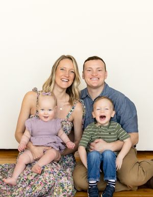 A family of four sits together against a white background, smiling and laughing joyfully.