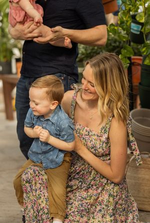 A parent and toddler share a playful moment in a garden setting, wearing coordinated denim and floral outfits.