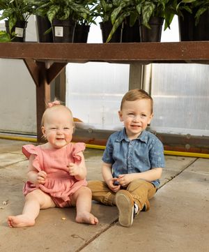 Two young children sitting on a concrete porch wearing pink and denim outfits while smiling and playing.