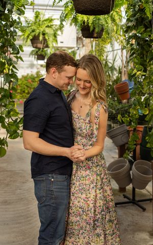 A couple shares an intimate moment in a greenhouse surrounded by lush greenery and potted plants.