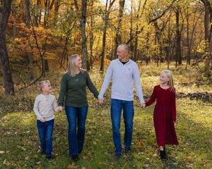 A family walks together through a sunlit autumn forest with golden leaves and warm afternoon light.