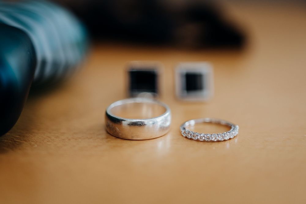 Two silver wedding bands and black square cufflinks arranged on a wooden surface for a wedding day detail shot.