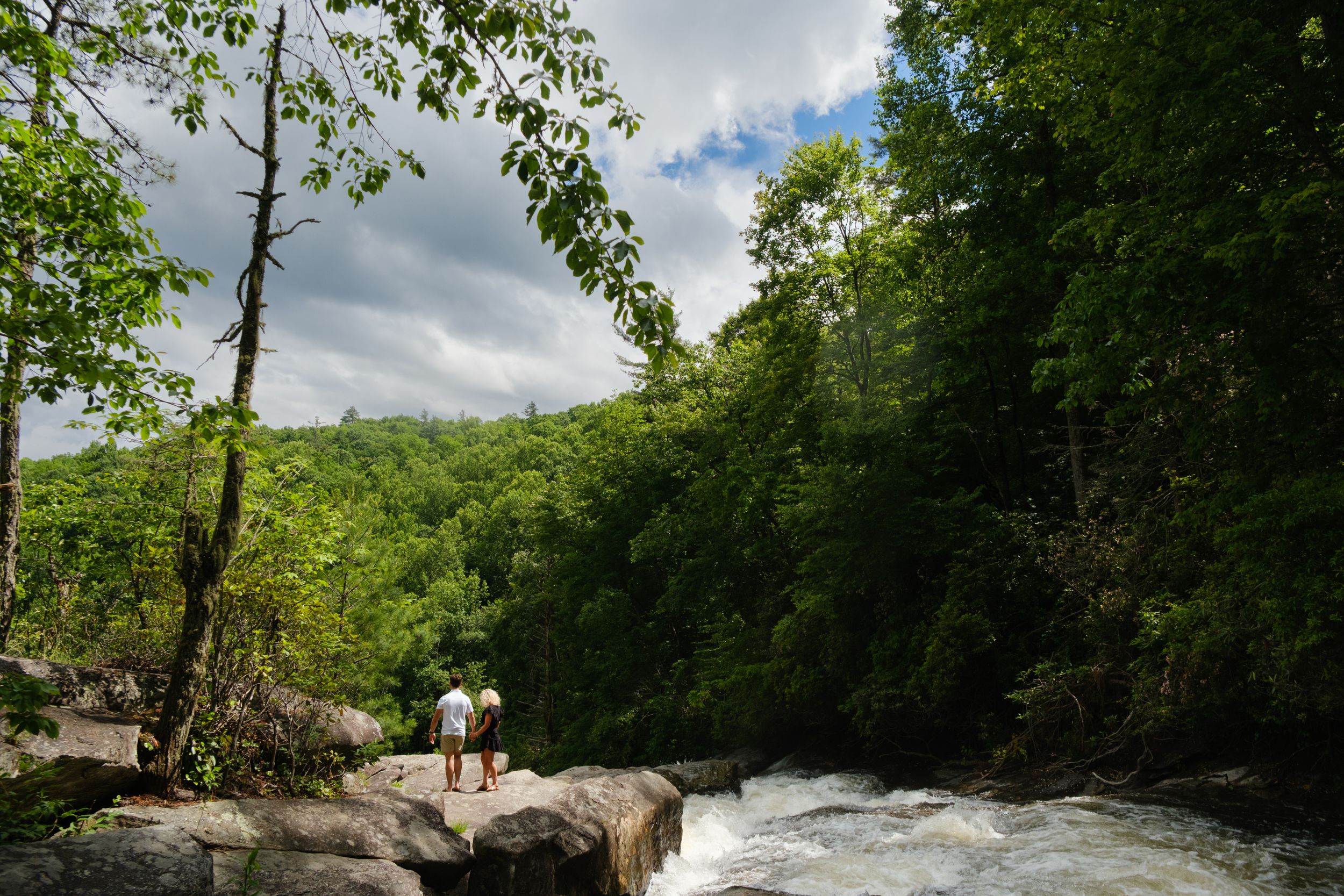 Wide Shot of the newly engaged couple hiking at the top of Rainbow Falls in Western North Carolina