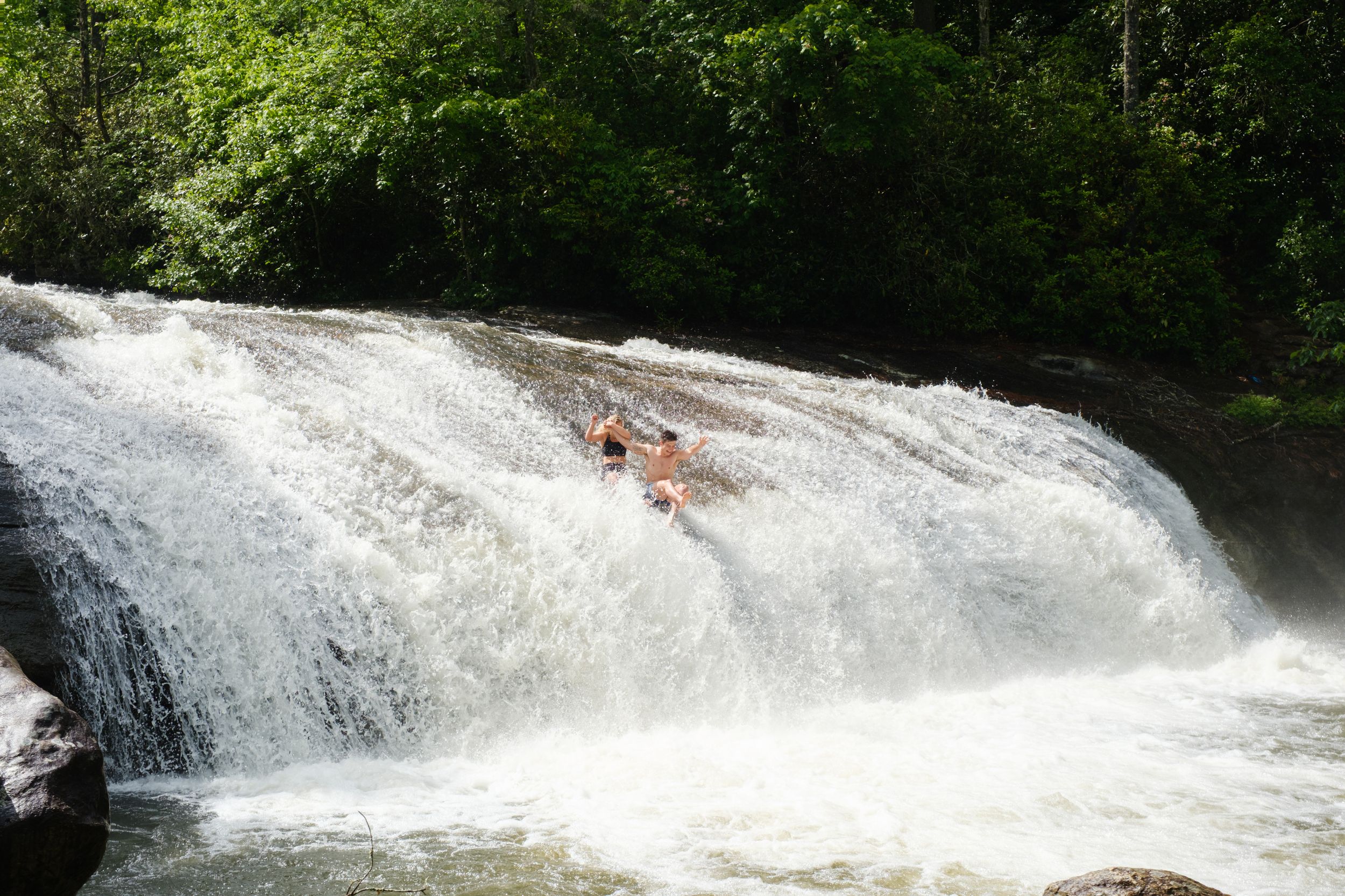 Couple sliding down Turtleback Falls after engagement session in North Carolina