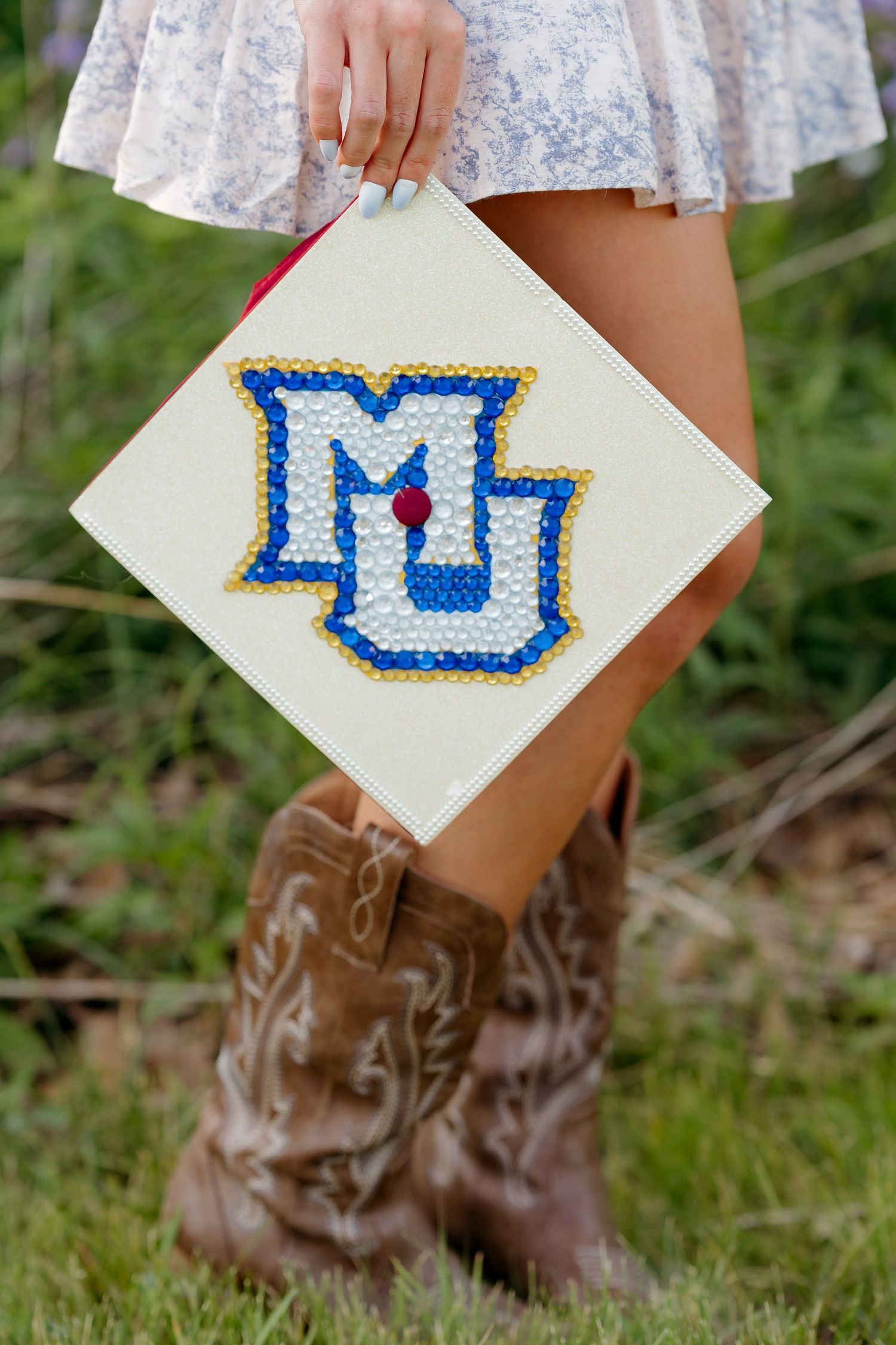 Woman in cowboy boots holding a bedazzled graduation cap featuring the MU Marquette University logo in blue and gold.
