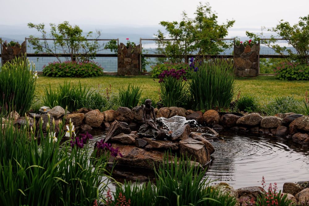 A serene garden pond surrounded by rocks, lush greenery, and colorful flowers with a scenic waterfront view.