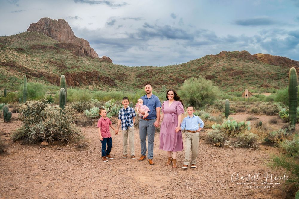 A family of five walks together through a scenic Arizona desert with saguaro cacti and red mountains.