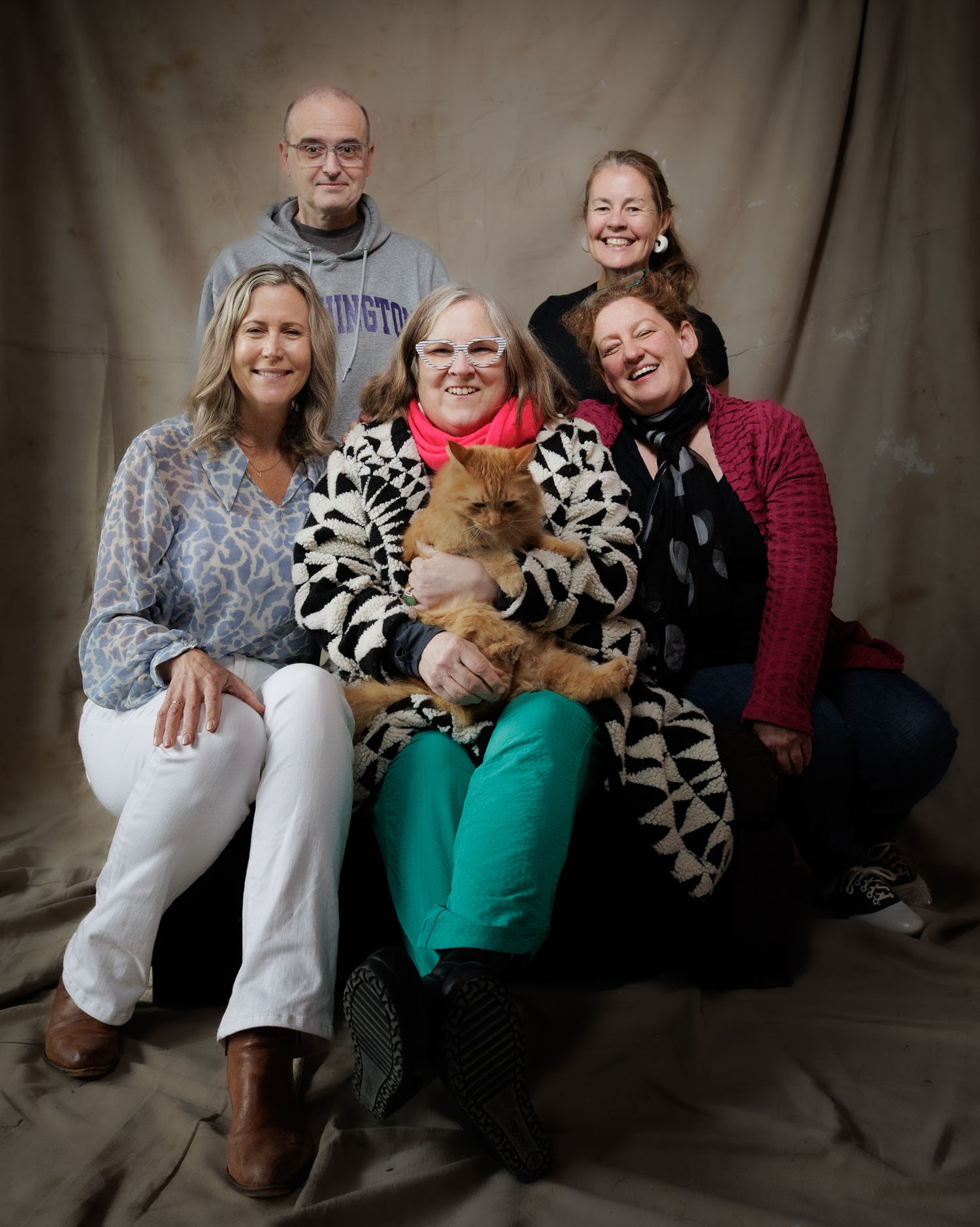 Family group portrait with five adults and an orange cat posing against a studio backdrop.
