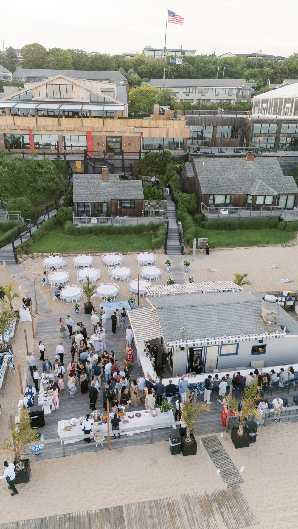 Aerial view of a beachfront wedding reception with white umbrellas and American flag.