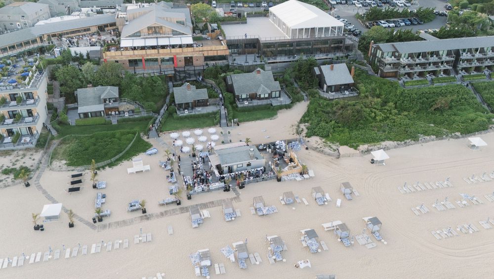 Aerial view of a beachfront resort with outdoor seating, beach chairs, and lush greenery along a sandy shoreline.