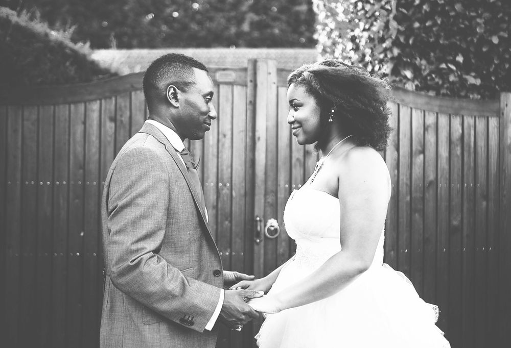 Black and white photo of a smiling bride and groom holding hands outdoors on their wedding day.