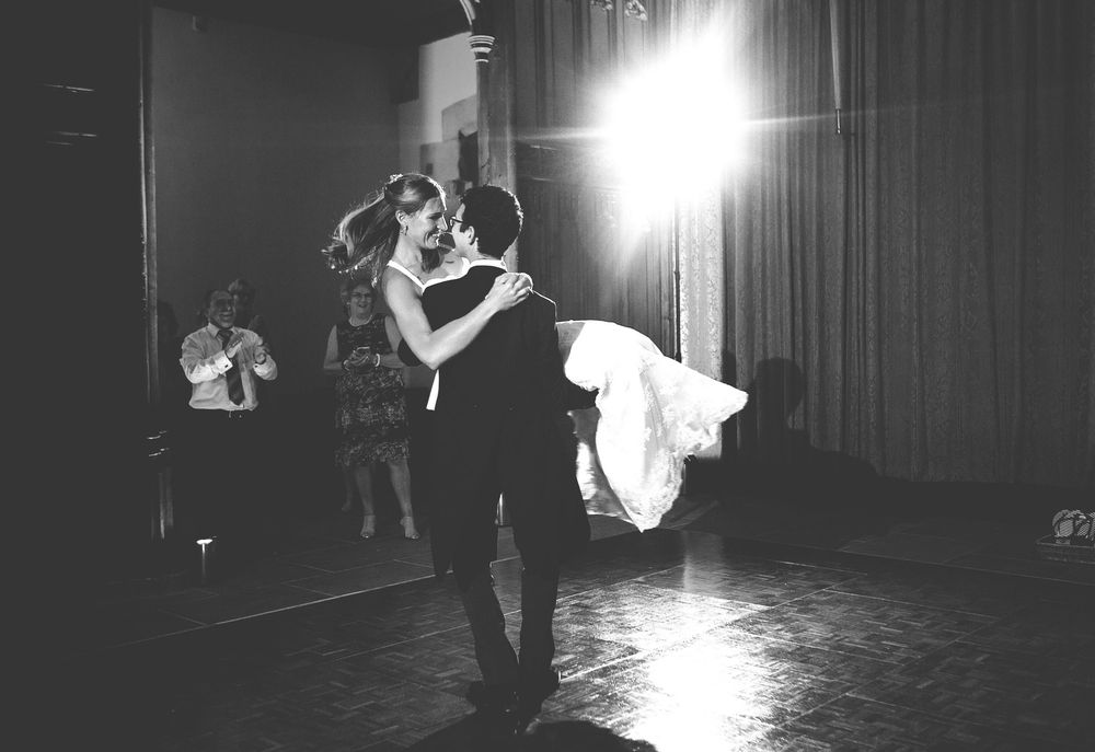 Black and white photo of a couple sharing their first dance at a wedding reception with a bright spotlight behind them.
