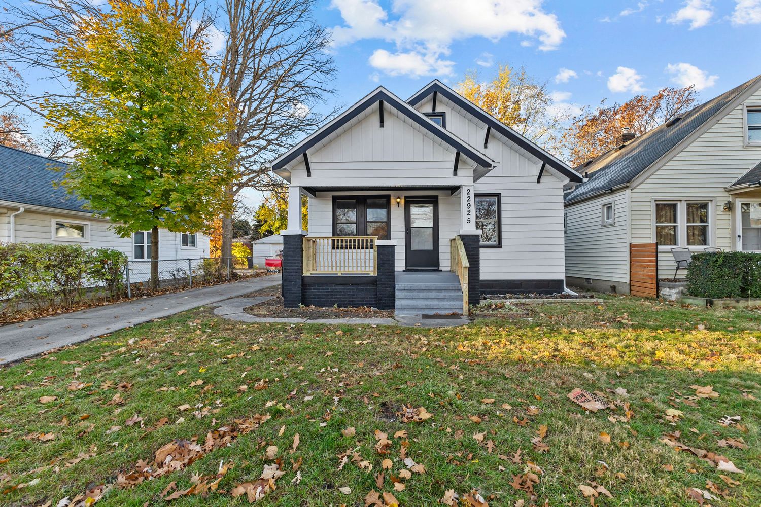 Charming stone cottage-style home with covered front porch, mature tree, and manicured green lawn.