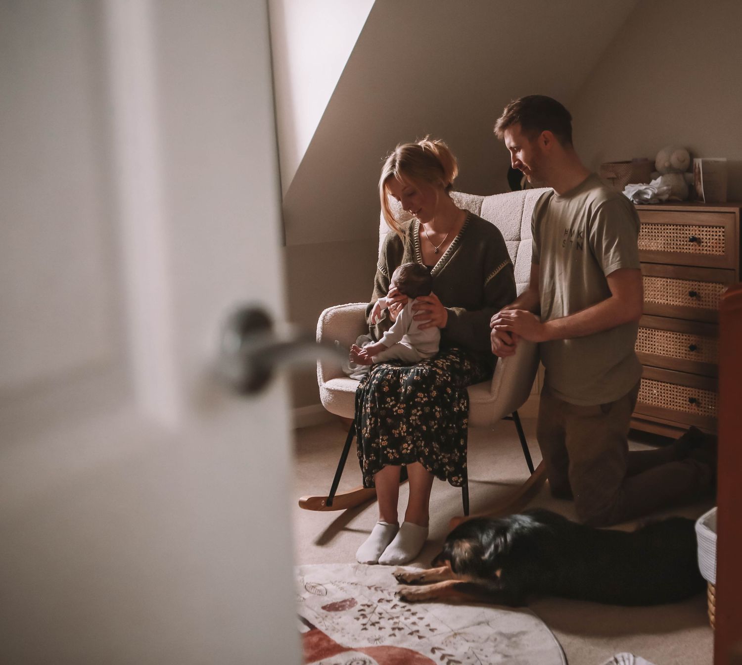 A couple sits together in a cozy nursery, tenderly holding their newborn baby in warm natural light.