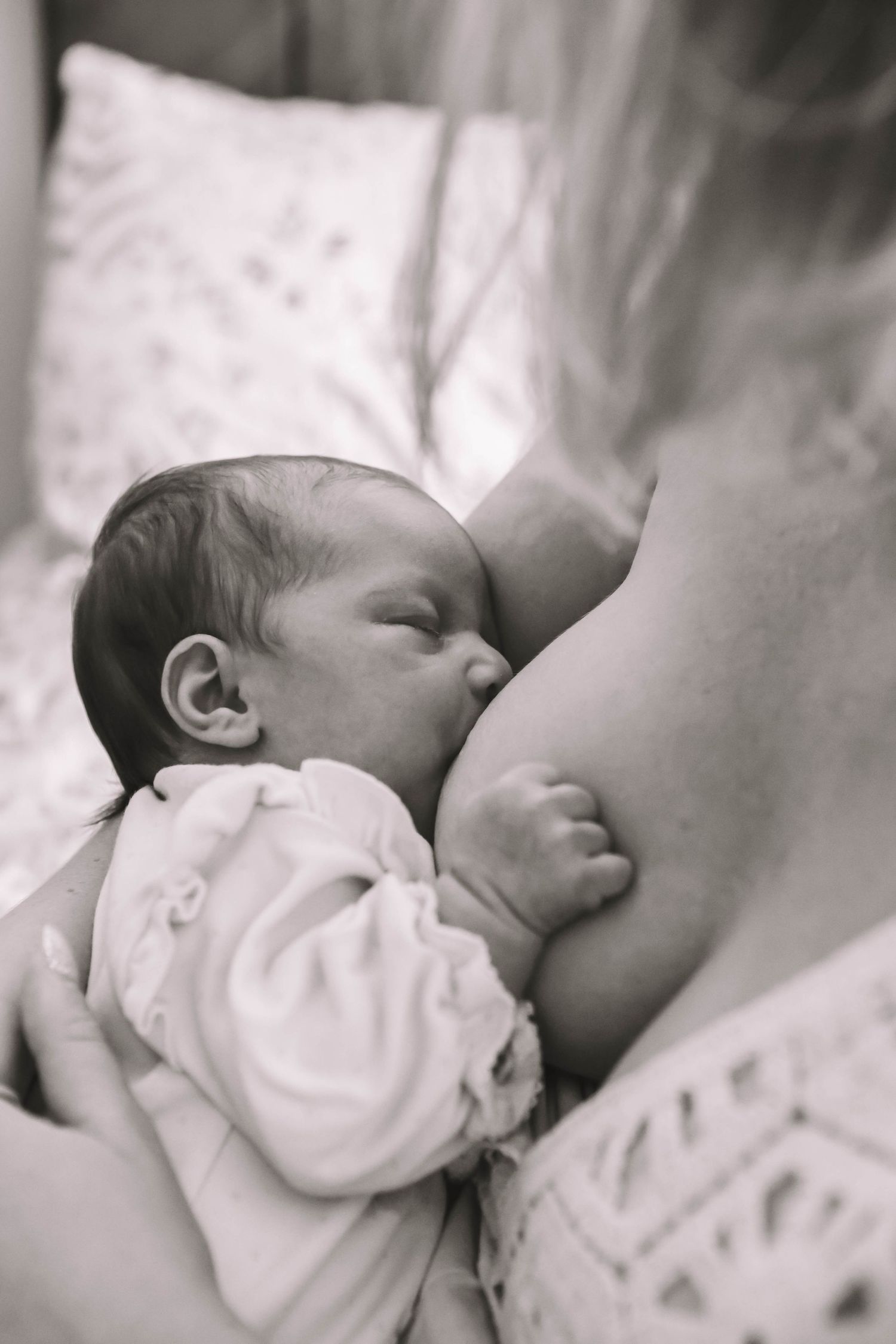 Black and white photo of a newborn baby breastfeeding, cradled in mother's arms.