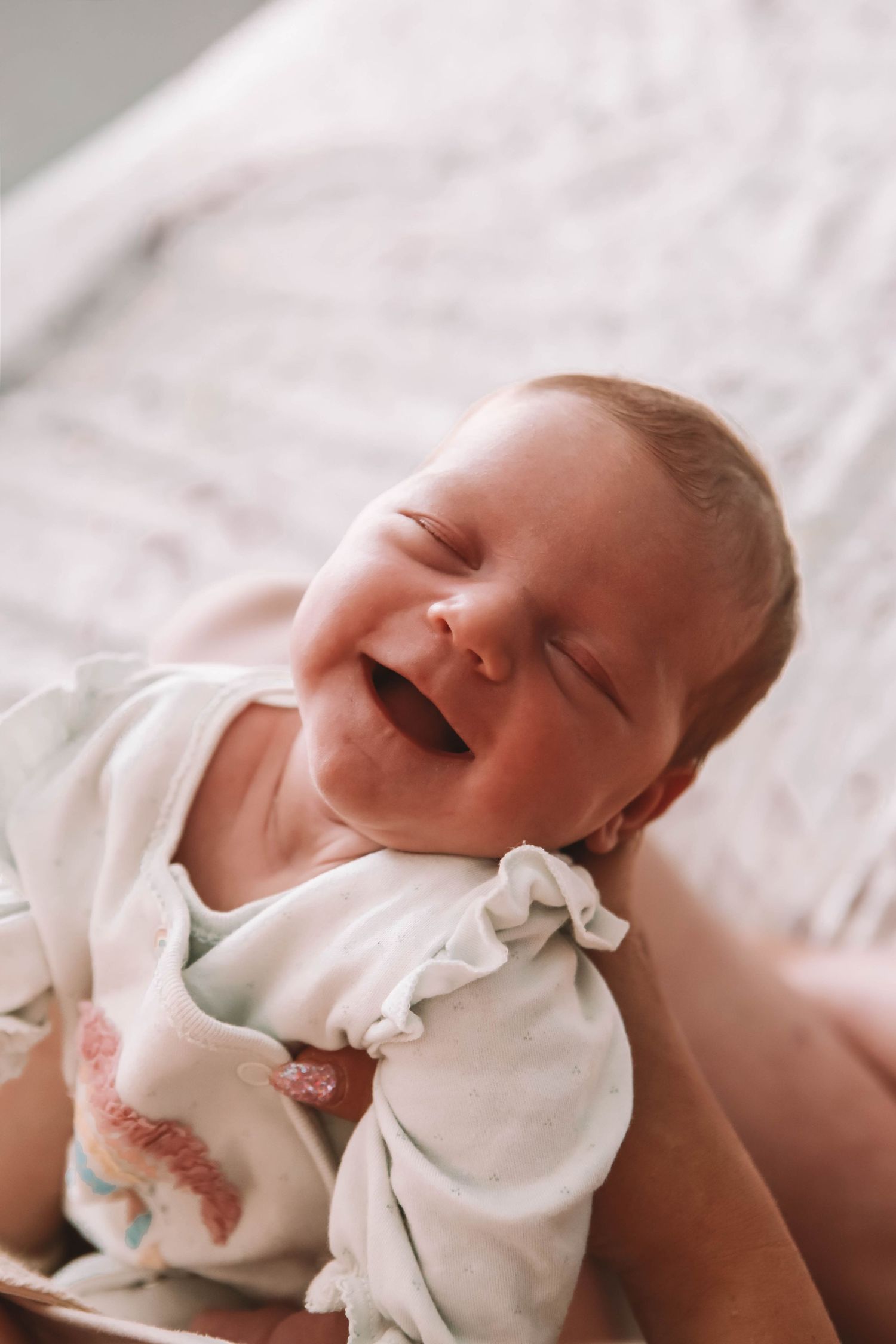 Adorable newborn baby smiling with eyes closed, dressed in white onesie, lying in a basket.