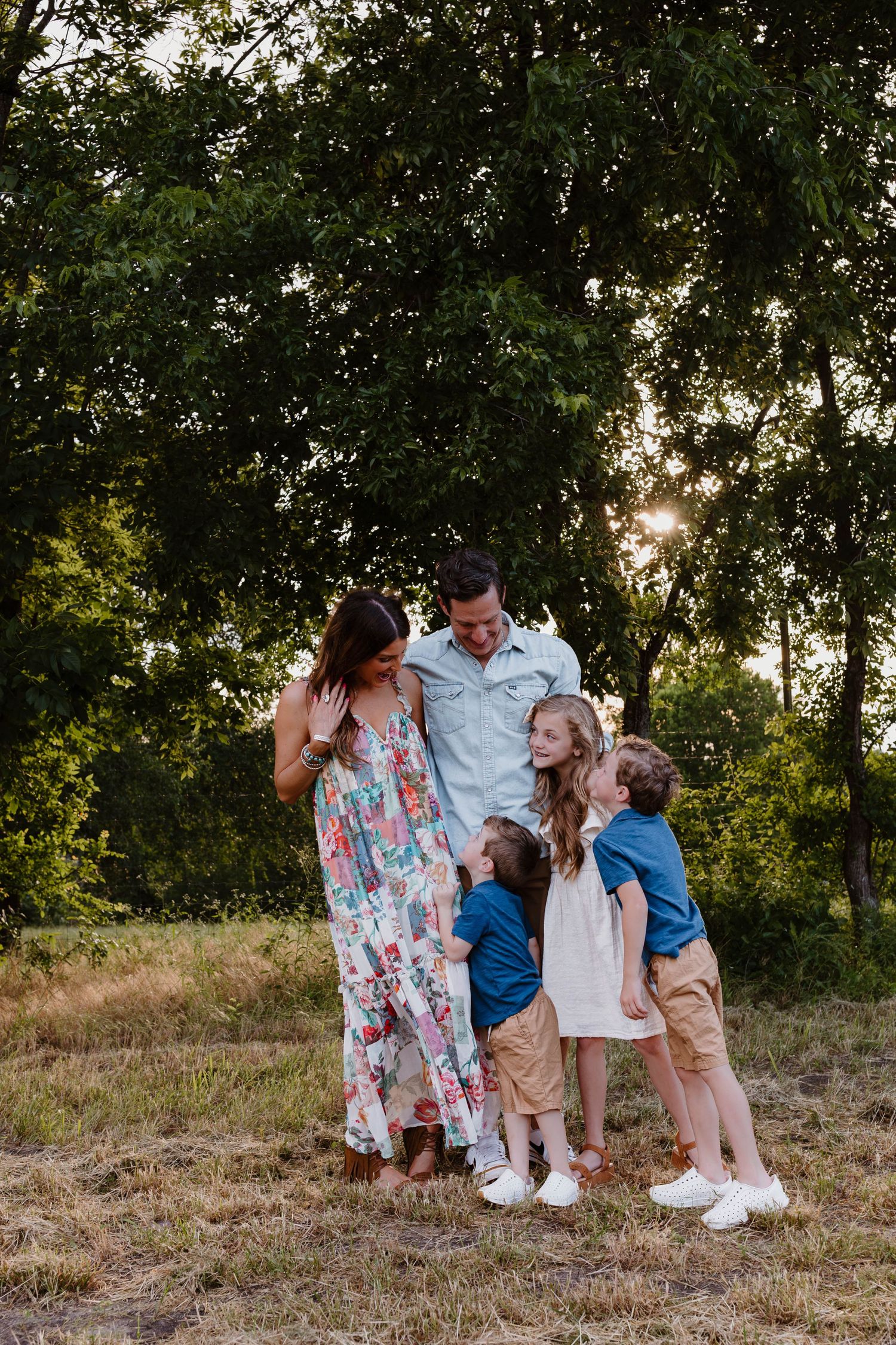 Happy family of five sharing a joyful moment outdoors at golden hour among lush green trees.