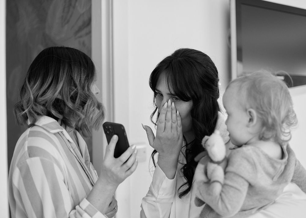 Black and white photo of two women reacting emotionally to a phone while holding a baby.