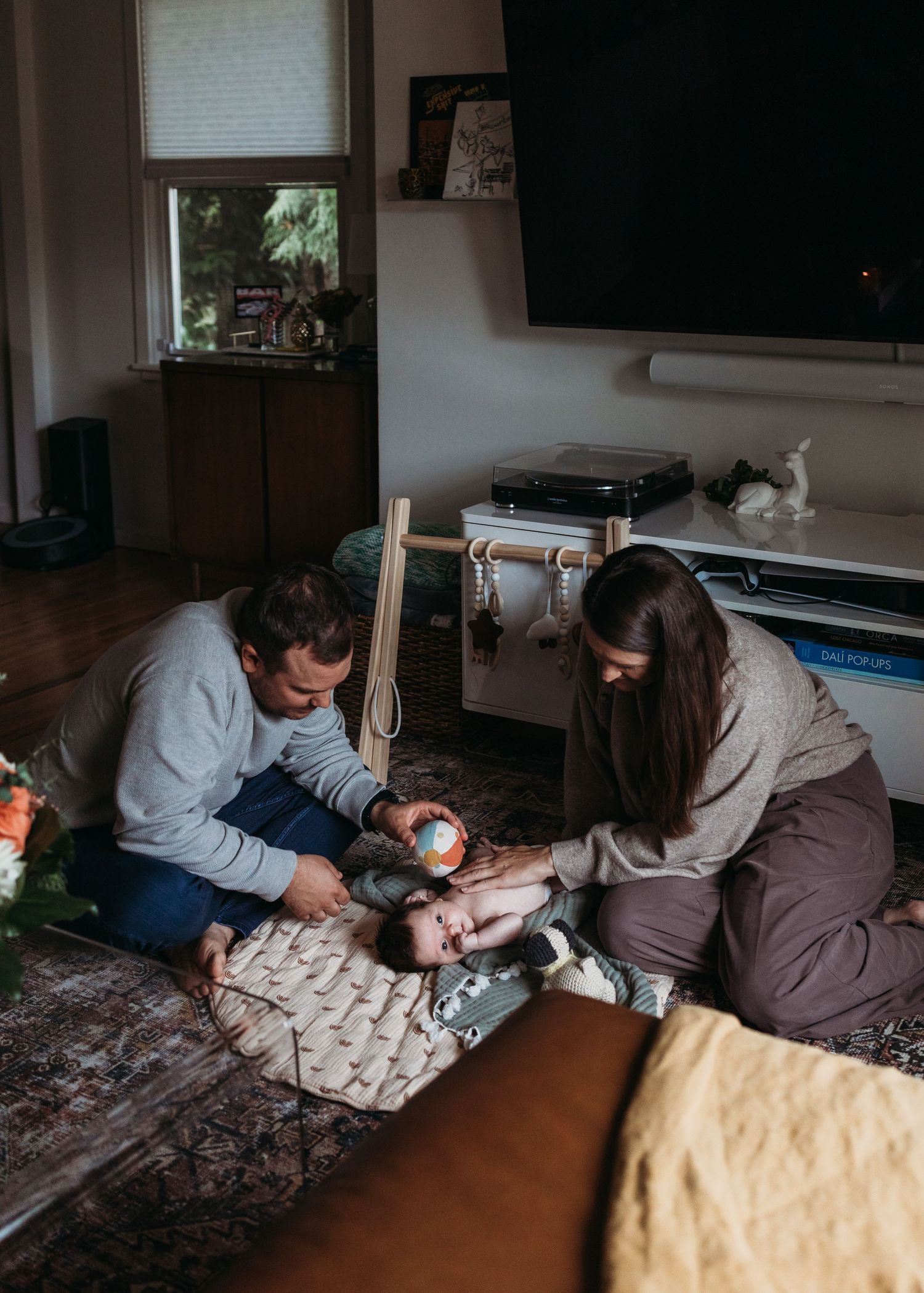 Parents sitting on floor with newborn baby on blanket in cozy living room home setting.