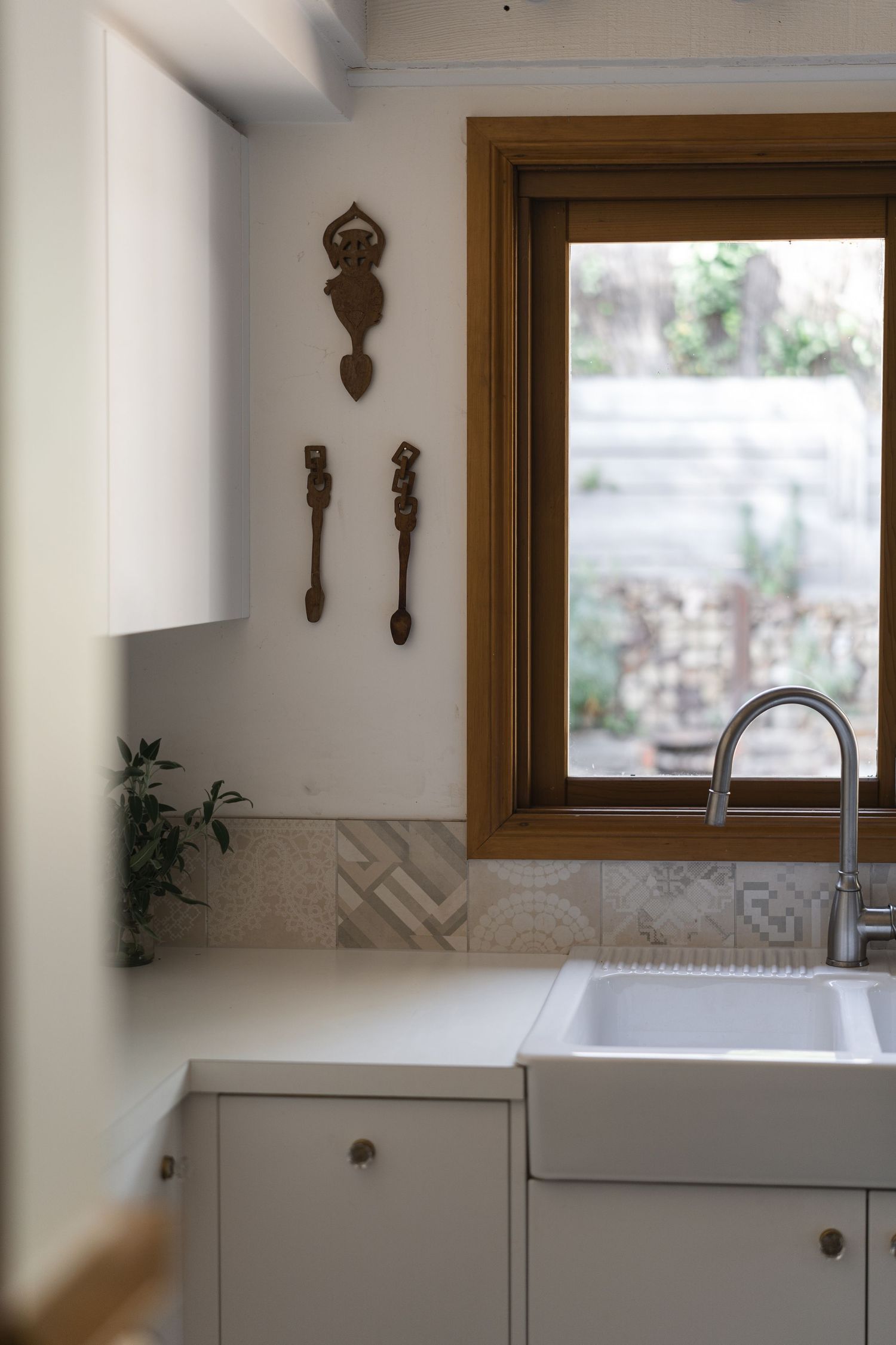 White kitchen with farmhouse sink, patterned tile backsplash, wooden window frame, and decorative wall spoons.

Rosey Knoll