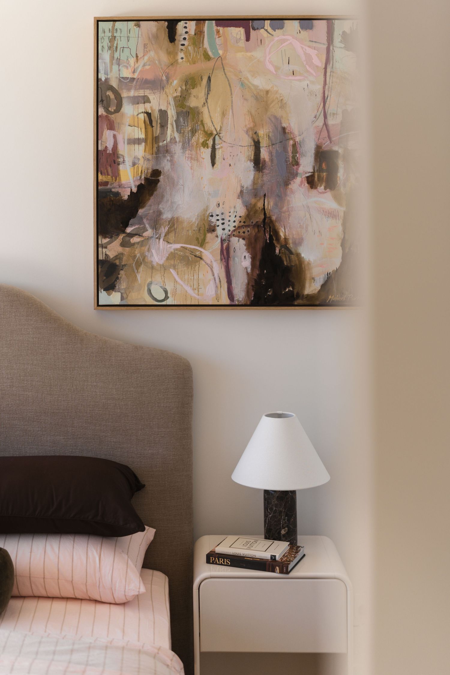 Bedroom corner with abstract pink and gold framed artwork above white nightstand with marble lamp and stacked books.

Middleton Fields