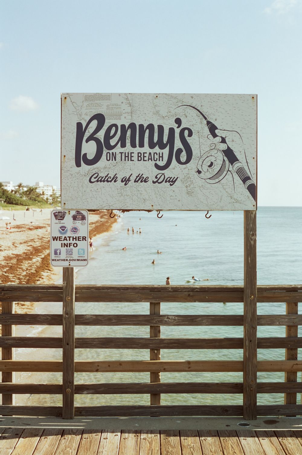 Benny's on the Beach sign with Catch of the Day slogan on a wooden pier overlooking a sunny Florida beach.