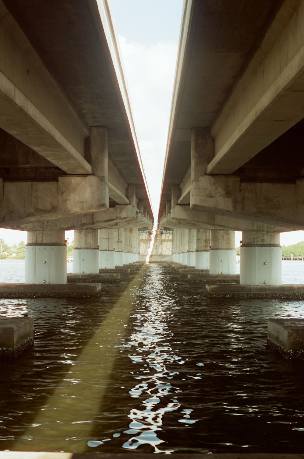 Symmetrical view under twin concrete highway bridges reflecting on dark water with converging perspective.