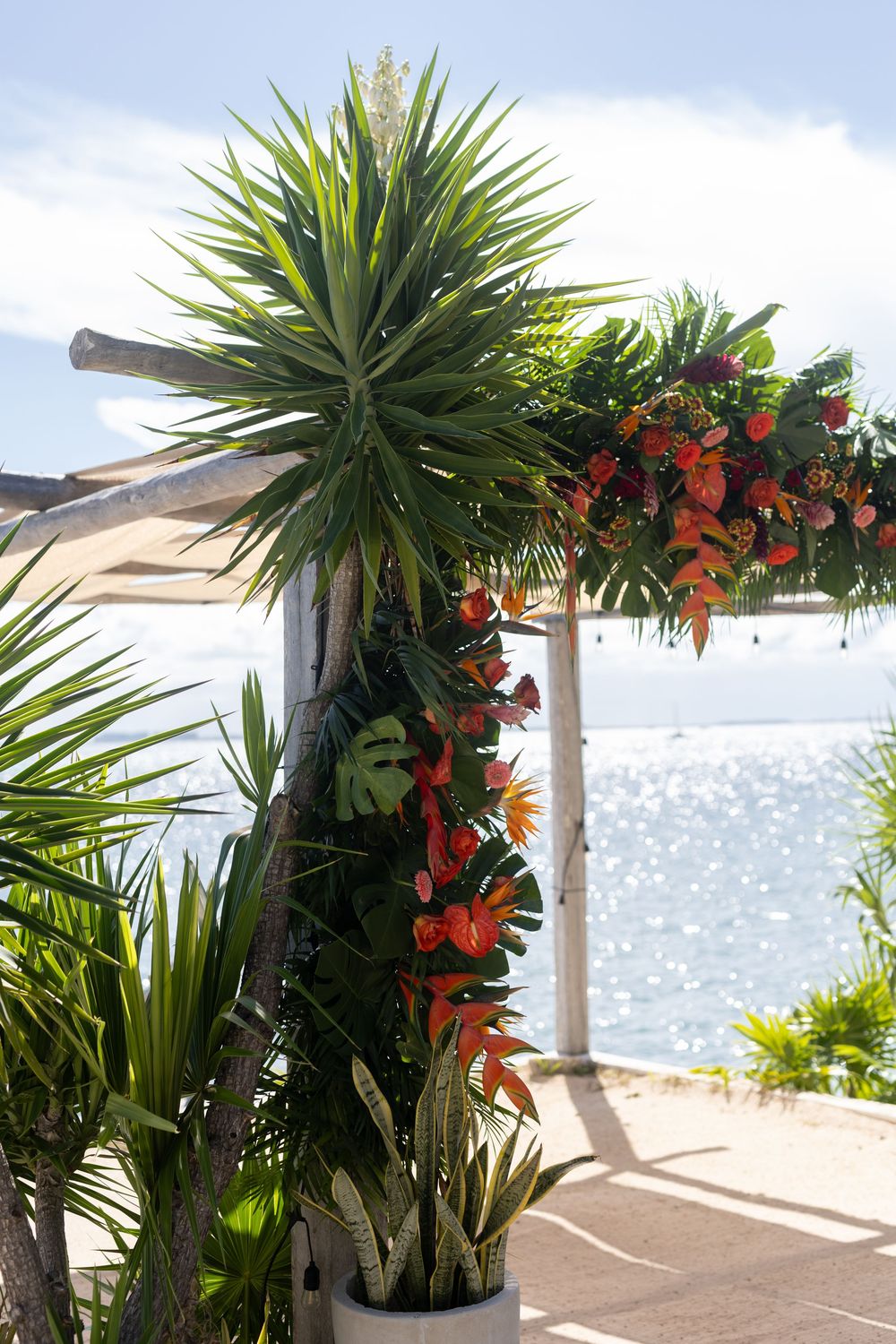Tropical floral arrangement with red anthuriums and palm leaves near a sparkling ocean at a beachside at Casa Coco, Isla Mujeres Mexico.