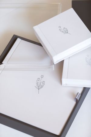 Elegant white stationery set with minimalist floral sketches, featuring notebooks and a pen on a dark tray.