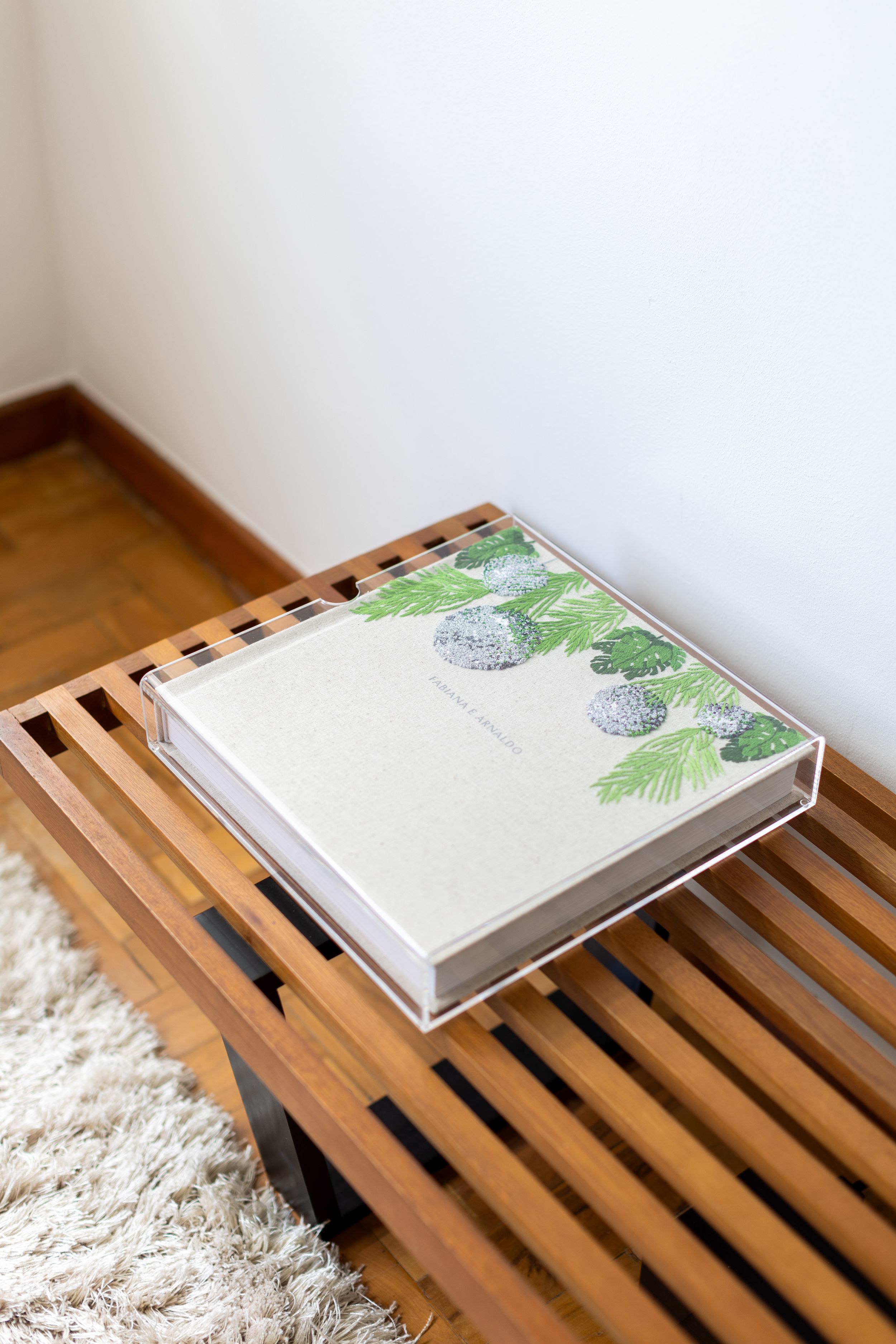 White hardcover book with green leaf design on wooden slat shelf photographed at three different angles.