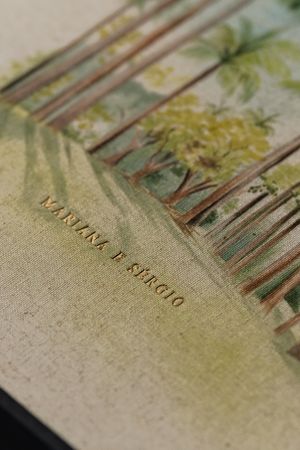 Close-up of a linen wedding album cover with gold foil names Martina and Sergio, featuring a tropical watercolor illustration.