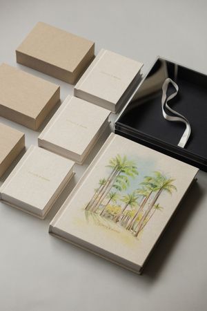 Elegant linen keepsake boxes with watercolor palm tree design, displayed with black gift box and ribbon.