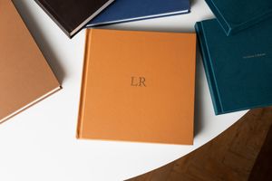 Elegant orange leather monogrammed LR journal surrounded by colorful hardcover notebooks on a white surface.