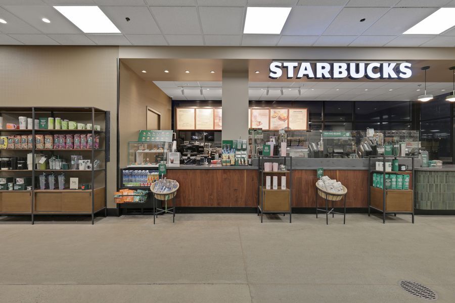 Starbucks coffee kiosk inside a retail store with product displays and seating area.