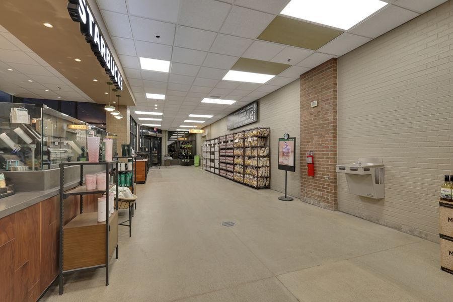 Interior of a mall corridor featuring a Starbucks coffee shop on the left and retail stores lining the hallway with tile flooring.