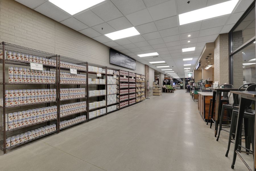 Modern retail store aisle with floor-to-ceiling product shelves, bright LED lighting, and polished concrete floors.
