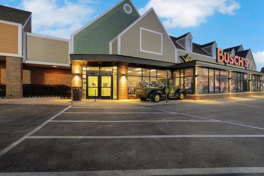 Busch's market storefront at dusk with empty parking lot and vintage military jeep displayed near entrance.