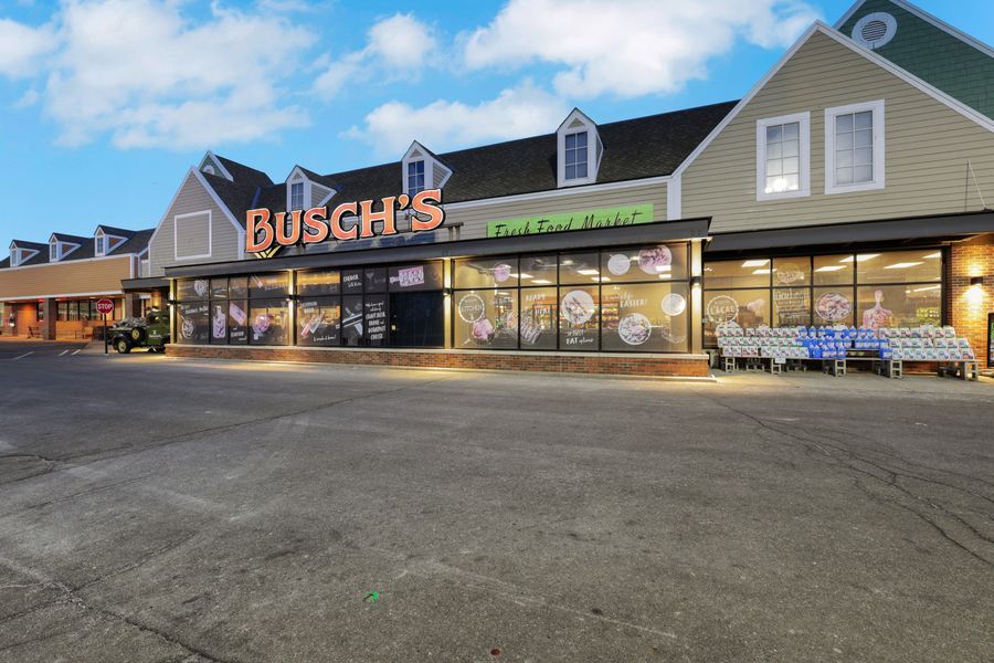 Busch's grocery store exterior with large parking lot at dusk, featuring illuminated signage and shopping carts.