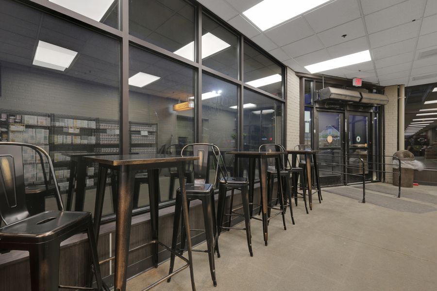 Modern bar seating area with black metal stools and floor-to-ceiling glass walls inside a retail store.