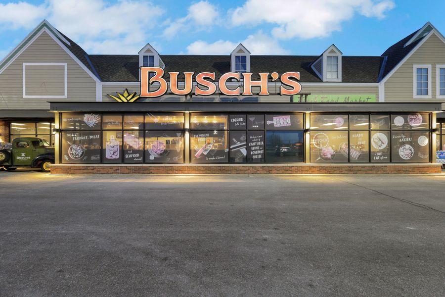 Exterior of Busch's Fresh Food Market at dusk with illuminated storefront and large display windows.