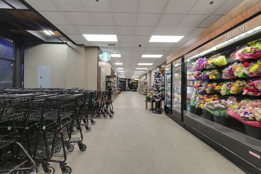 Grocery store entrance with rows of black shopping carts beside refrigerated floral displays and a Starbucks cafe.