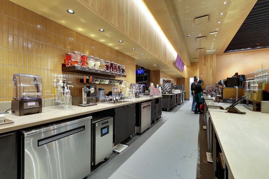 Commercial coffee bar interior featuring stainless steel equipment, yellow tile backsplash, and beverage dispensers on counter.